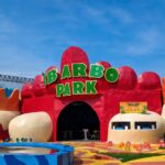 Colorful amusement park entrance with a large green 'IBARBO PARK' sign atop red archways and a flower-adorned path.