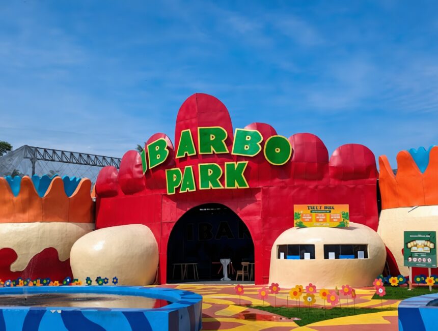 Colorful amusement park entrance with a large green 'IBARBO PARK' sign atop red archways and a flower-adorned path.