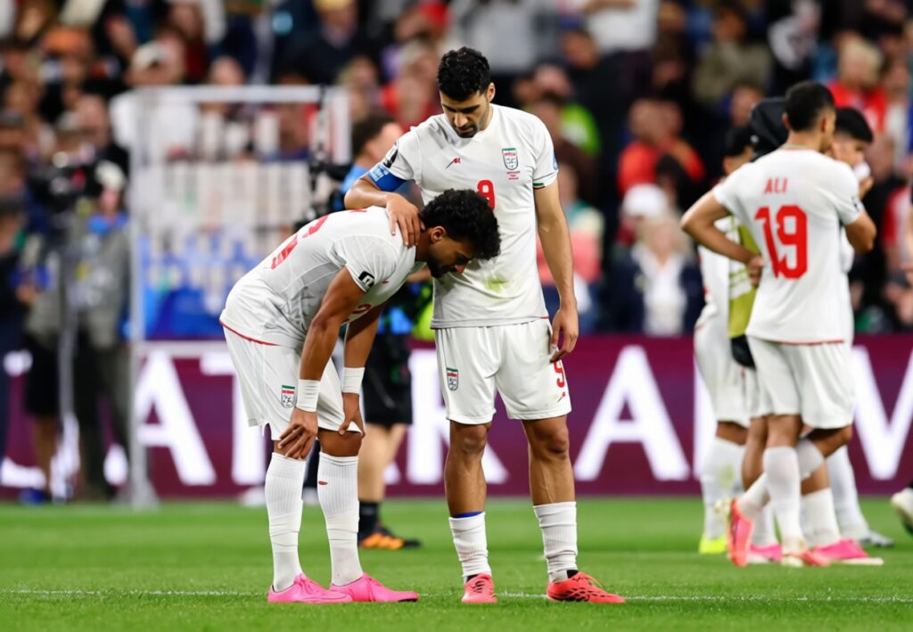 Iran dejected after wc draw with egypt by REUTERS FIXX - Mabur.co Two Iran soccer players in white uniforms bend over on the field, one resting a hand on the other’s shoulder in a moment of camaraderie amid a crowded stadium.