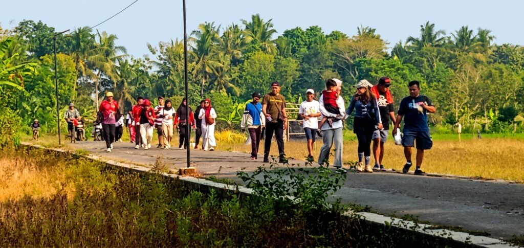 Group of people walking along a rural road with palm trees in the background, sunny day.
