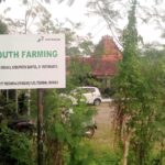Large outdoor sign reading 'JOGJA YOUTH FARMING' with logos, surrounded by green plants and trees; a building with a red-tiled roof visible in the background