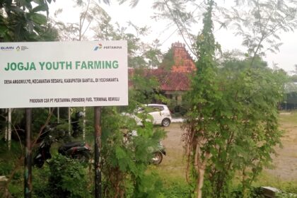 Large outdoor sign reading 'JOGJA YOUTH FARMING' with logos, surrounded by green plants and trees; a building with a red-tiled roof visible in the background