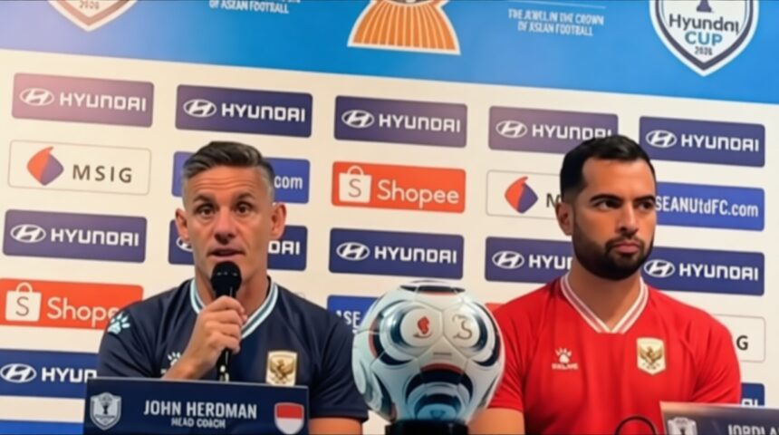 Press conference scene: John Herdman (Head Coach) speaks into a microphone beside a red-shirted teammate, with a soccer ball on the table and sponsor logos in the background.