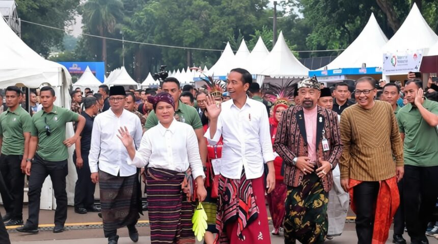 Jokowi festival sarung 2019 by Sekretariat presiden YT FIXX - Mabur.co A group of officials and attendees in traditional Indonesian clothing wave as they walk past a crowd under white festival tents.