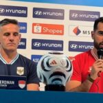 Press conference with head coach John Herdman (left) and player Jordi Amat (right) beside a soccer ball, sponsor backdrop.