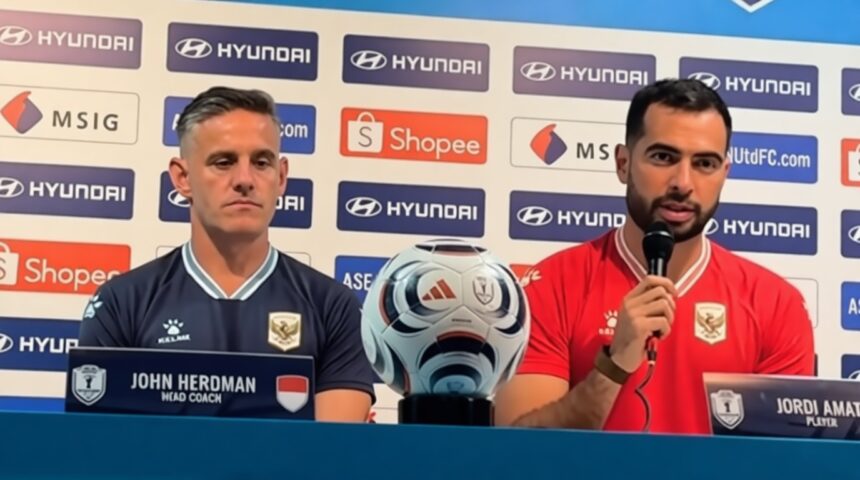 Press conference with head coach John Herdman (left) and player Jordi Amat (right) beside a soccer ball, sponsor backdrop.