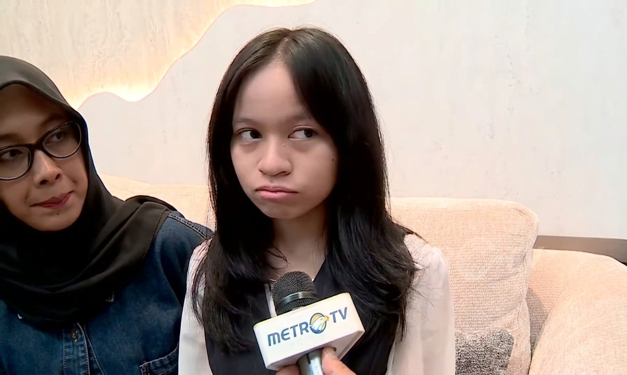 Young woman seated on a beige sofa during a Metro TV interview, holding a microphone close to her face.