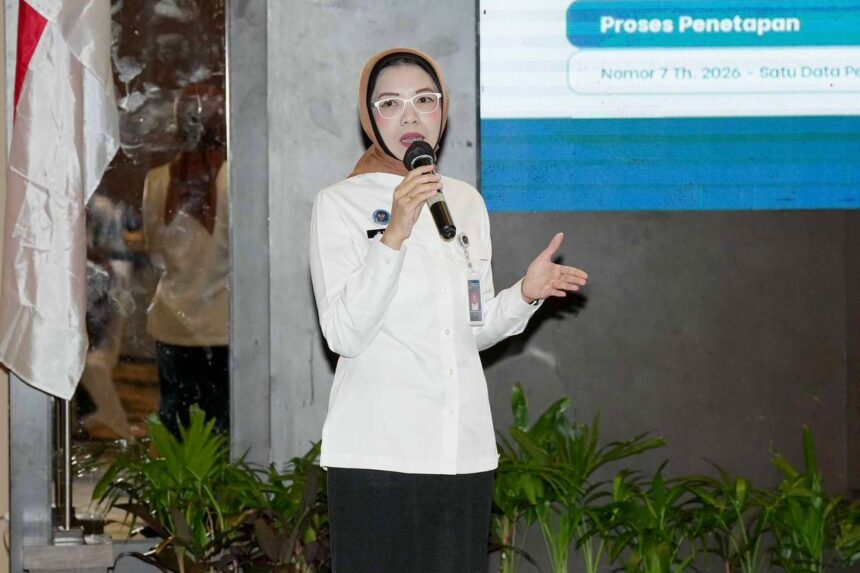 Woman wearing a hijab and glasses speaks into a handheld microphone on stage during a presentation.