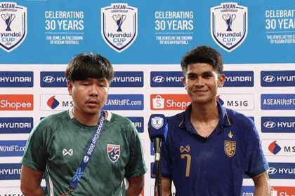 Two football players answer questions at a press conference, backdrop filled with Hyundai and ASEAN logos; one in green jersey with lanyard, the other in blue with number 7 smile behind a microphone.
