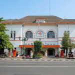 White colonial-style Pos Indonesia post office building with red-orange trim and arched windows on a sunny street.