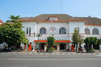 White colonial-style Pos Indonesia post office building with red-orange trim and arched windows on a sunny street.