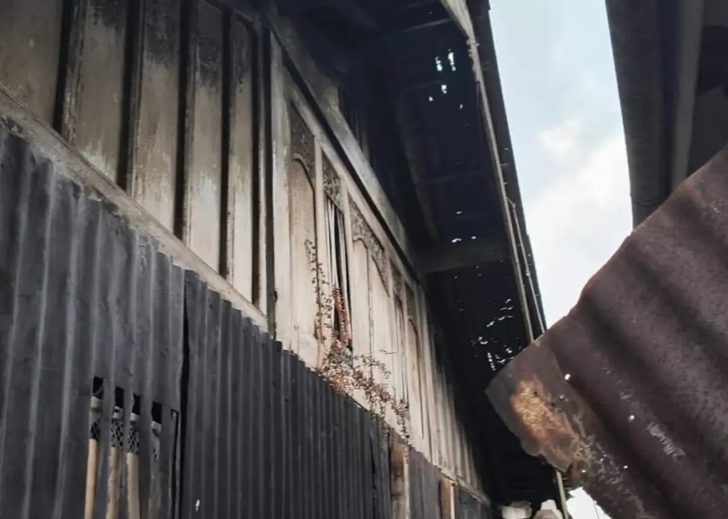 Fire-damaged building exterior with charred siding, soot and a rusted metal roof.