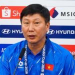 Man in a blue polo speaking into a microphone at a press conference, backdrop with sponsor logos and a Vietnamese flag on his chest.