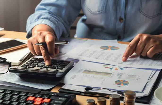 Person in a denim shirt uses a calculator and reviews financial charts on a desk