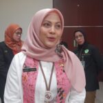 Close-up of a woman in a pink hijab and white shirt at an indoor event, name badge visible on her chest.