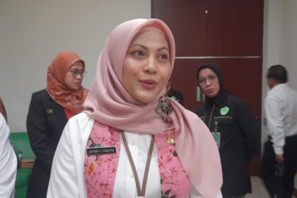 Close-up of a woman in a pink hijab and white shirt at an indoor event, name badge visible on her chest.
