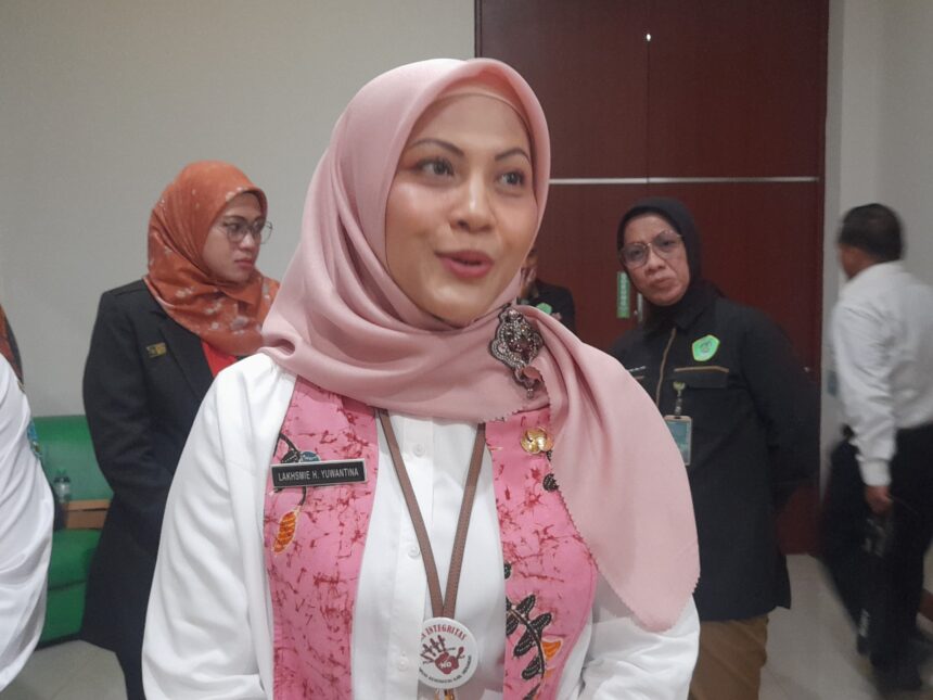 Close-up of a woman in a pink hijab and white shirt at an indoor event, name badge visible on her chest.
