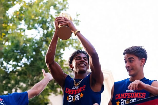 Three young men in blue jerseys celebrate on a parade float; the center player raises a trophy overhead.",