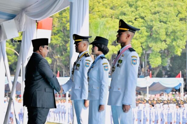 Man in a black suit shakes hands with a female officer and two male officers in light-blue dress uniforms during a formal ceremony under a tent.