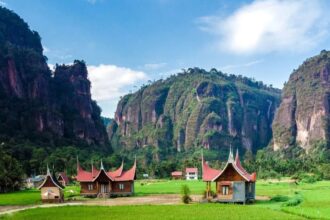 Rice fields and traditional wooden houses with curved red roofs, framed by tall karst cliffs.