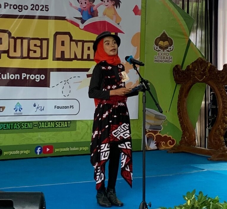 Lomba baca puisi anak Nov 2025 by Regas 2 - Mabur.co Girl in a red hijab and black outfit delivering a performance on a blue stage with a microphone in front of a colorful banner.