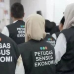Group of census officers wearing black vests with 'PETUGAS SENSUS EKONOMI' seen from the back.