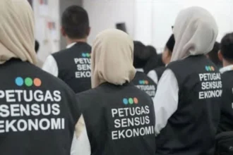 Group of census officers wearing black vests with 'PETUGAS SENSUS EKONOMI' seen from the back.