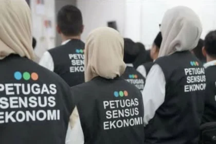 Group of census officers wearing black vests with 'PETUGAS SENSUS EKONOMI' seen from the back.