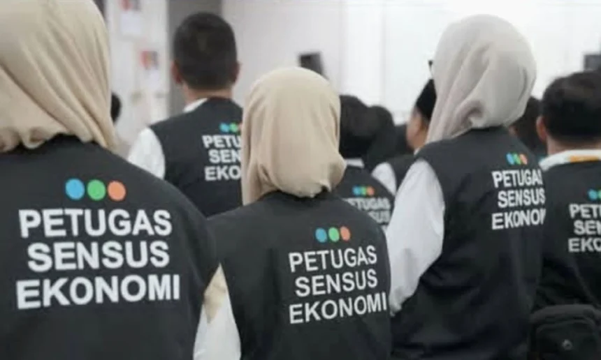 Group of census officers wearing black vests with 'PETUGAS SENSUS EKONOMI' seen from the back.