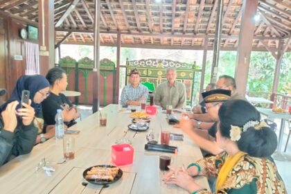 Group of people seated around a long wooden table in an open-air pavilion, sharing snacks and drinks.