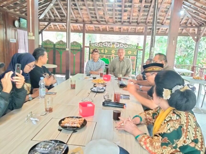 Group of people seated around a long wooden table in an open-air pavilion, sharing snacks and drinks.