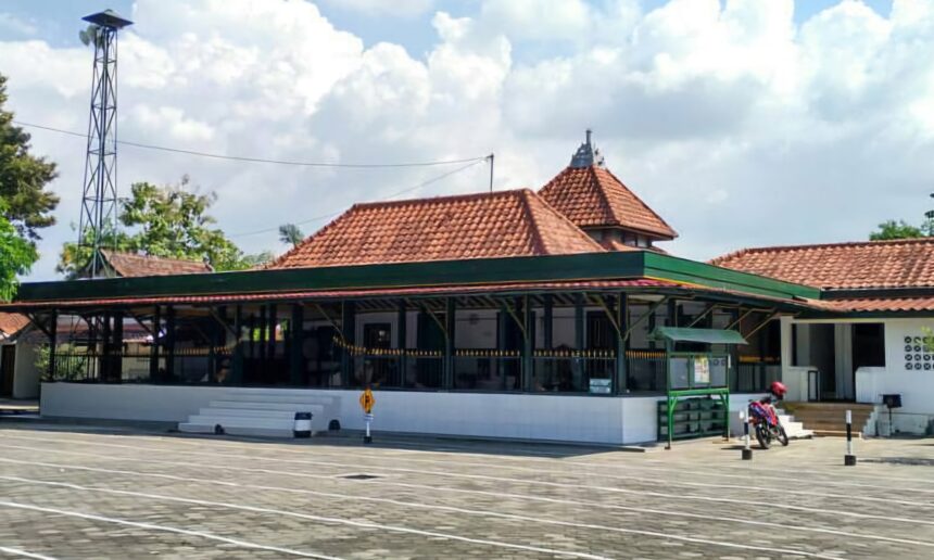 Temple-style building with red tiled roofs and white walls in a paved open area; a motorcycle parked on the right side.