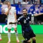 Argentina's Lionel Messi celebrates a goal with arms outstretched as England players in white react in the background.