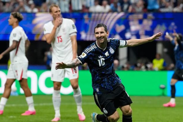 Argentina's Lionel Messi celebrates a goal with arms outstretched as England players in white react in the background.