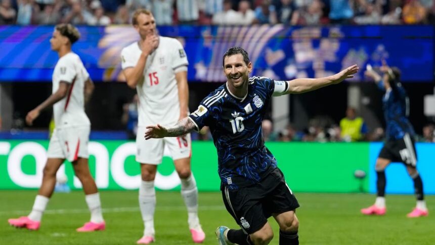 Argentina's Lionel Messi celebrates a goal with arms outstretched as England players in white react in the background.