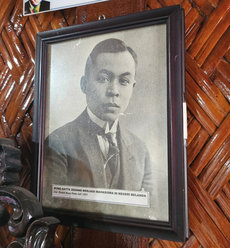 Mohammad-Hatta_Hattahouse_foto_interieur_6_Sumatra_maart2025_Feba-Sukmana - Mabur.co Framed black-and-white portrait of a young man in a suit; Indonesian caption mentions Bung Hatta studying in the Netherlands (1995).