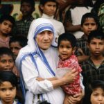 Older woman in a white and blue sari holding a young child, surrounded by curious children onlookers