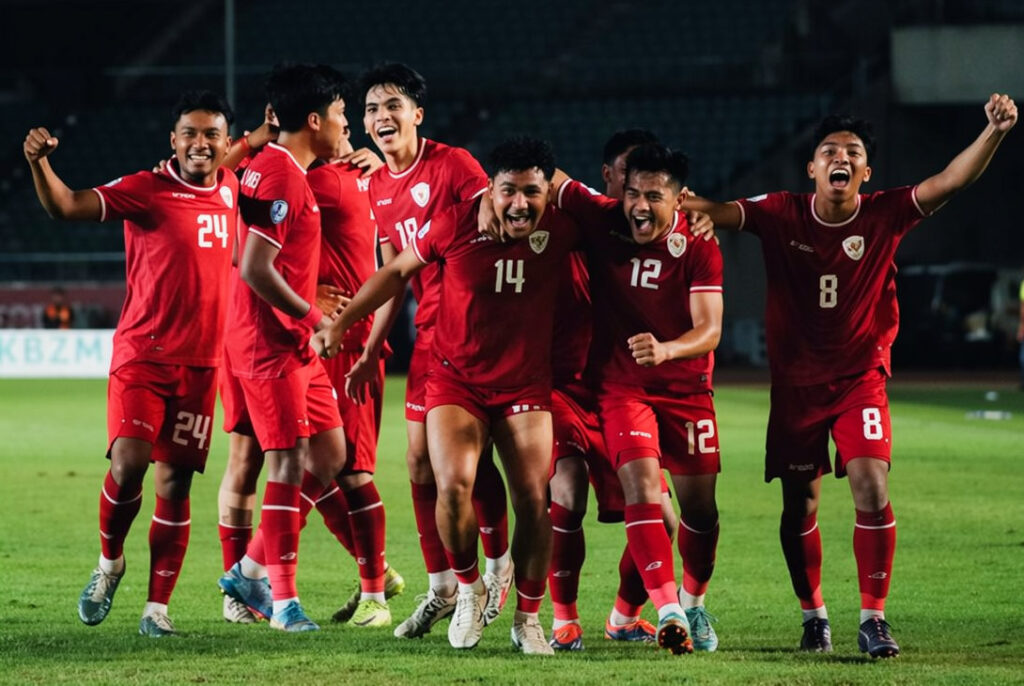 Myanmar 0-1 Indonesia AFF 2024 FIXX - Mabur.co A group of soccer players in red jerseys celebrate on a green pitch at night, with arms around each other in a triumphant moment.