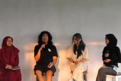 Four women panelists seated on stage during a discussion; one speaker holds a microphone while others listen.