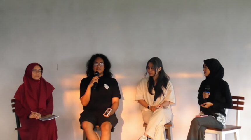 Four women panelists seated on stage during a discussion; one speaker holds a microphone while others listen.