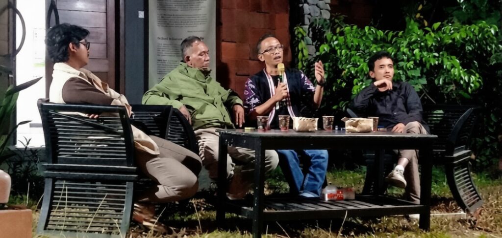 Panel discussion outdoors with four people seated around a table with cups and snacks on a bench and chairs nearby.