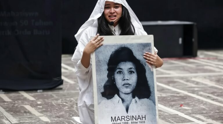 Young woman in white clothes holding a large portrait of Marsinah at a protest rally