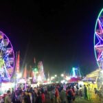 Night carnival scene with colorful neon Ferris wheels and a crowded fairground at dusk/darkness