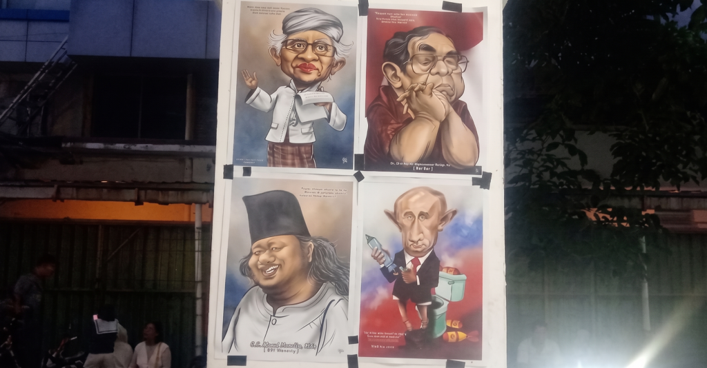Outdoor display board with four caricature posters of politicians, taped to a white panel beside a fence and trees. The drawings exaggerate facial features and poses for humorous effect, arranged in a 2x2 grid.