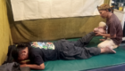 Man lying face down on a mat while another person holds and bends his leg in a training or therapy setting.