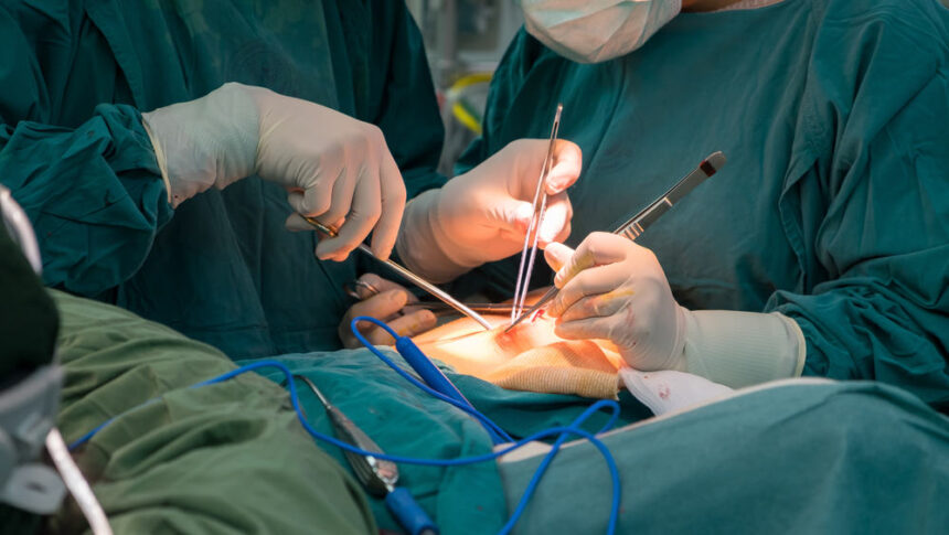 Surgeons in sterile green gowns performing an operation with scalpels and forceps at the patient’s incision site.