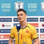 Vietnamese footballer in a yellow jersey speaks into a microphone at a press conference, with sponsor banners and a turquoise backdrop displaying ASEAN/Hyundai Cup logos.