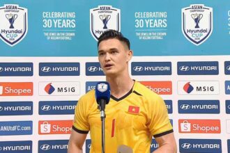 Vietnamese footballer in a yellow jersey speaks into a microphone at a press conference, with sponsor banners and a turquoise backdrop displaying ASEAN/Hyundai Cup logos.