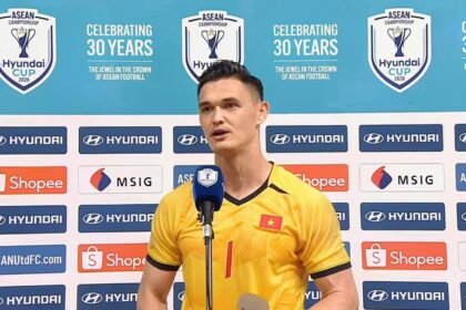 Vietnamese footballer in a yellow jersey speaks into a microphone at a press conference, with sponsor banners and a turquoise backdrop displaying ASEAN/Hyundai Cup logos.