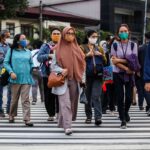 Diverse group of pedestrians wearing masks crossing a city crosswalk together.
